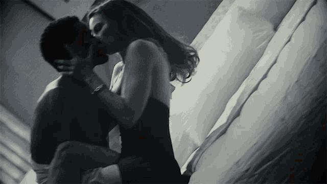 a man and woman kissing on a bed with white sheets