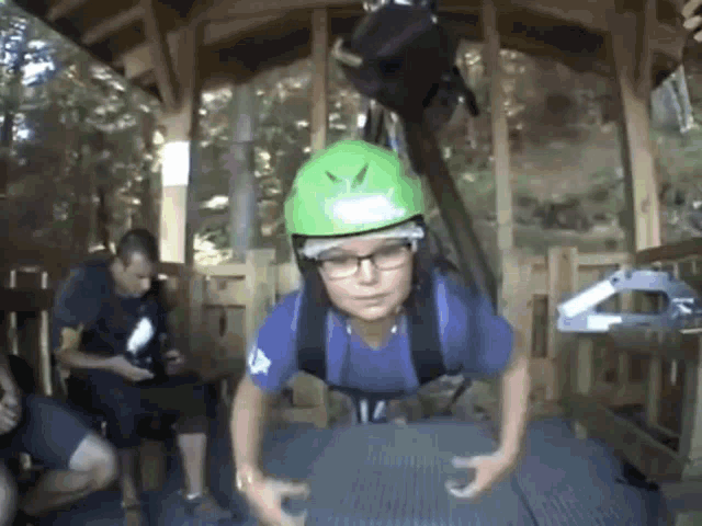 a boy wearing a green helmet and glasses is doing push ups while a man watches .