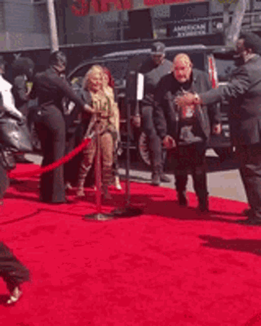 a woman is walking on a red carpet with a man standing behind her