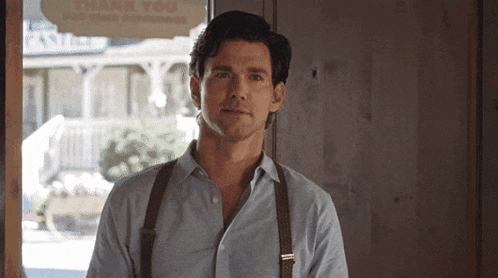 a man wearing suspenders is standing in front of a window that says thank you