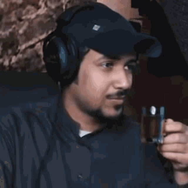 a man wearing headphones and a hat with the letter r on it drinks from a cup