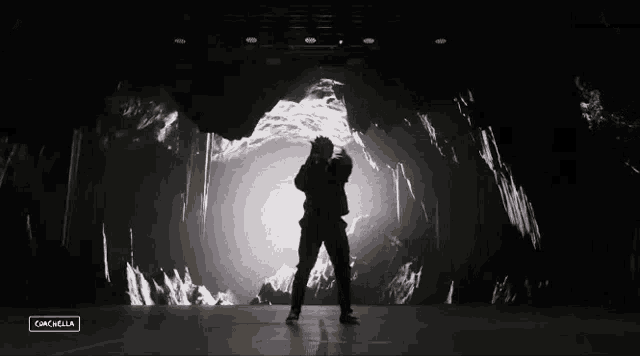 a black and white photo of a man dancing in front of a large screen that says ' campella ' on it