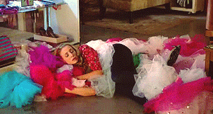 a woman is laying on the floor surrounded by a pile of colorful dresses