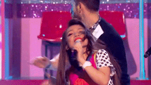 a woman is singing into a microphone while a man watches .