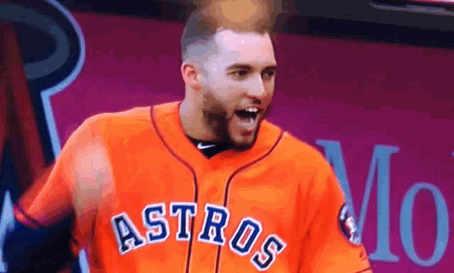a man wearing an orange astros jersey is standing in front of a pink wall