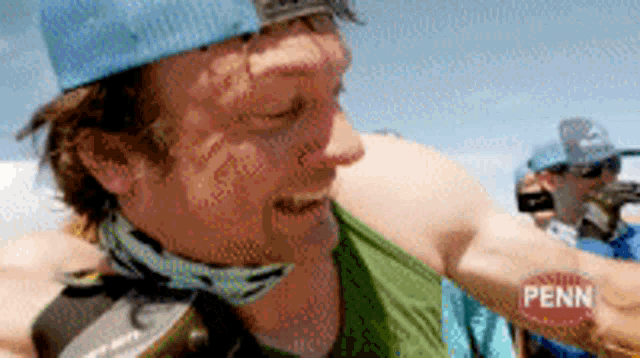 a man wearing a green tank top and a blue hat is holding a penn fishing rod