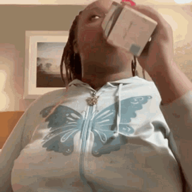 a woman wearing a butterfly hoodie is drinking from a bottle .