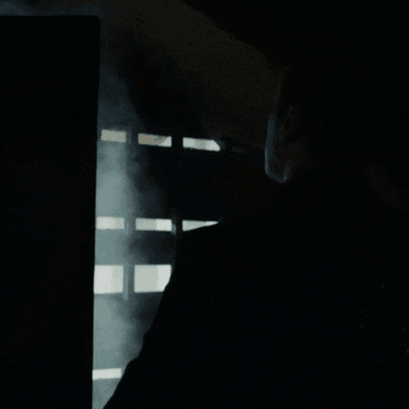 a man in a black suit looks out a window with smoke coming out of it