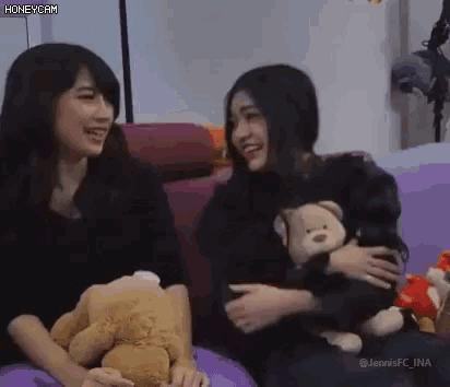 two girls are sitting on a couch holding teddy bears and smiling .