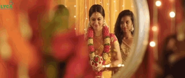 a bride is looking at her reflection in a mirror while holding a garland of flowers .
