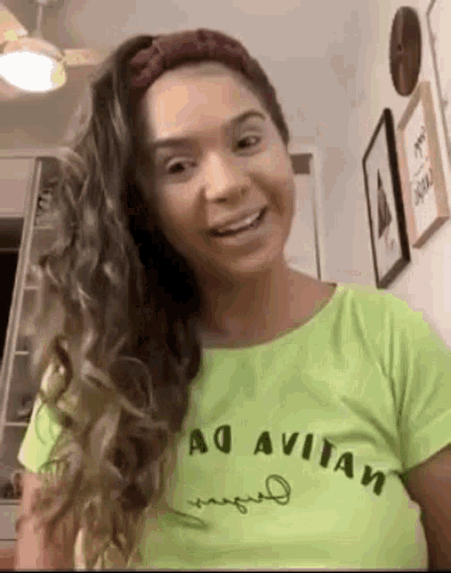 a woman wearing a green t-shirt and a headband is smiling and looking at the camera .
