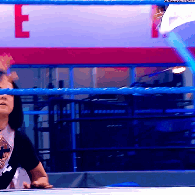 a woman stands in a wrestling ring with the letter e on the wall behind her