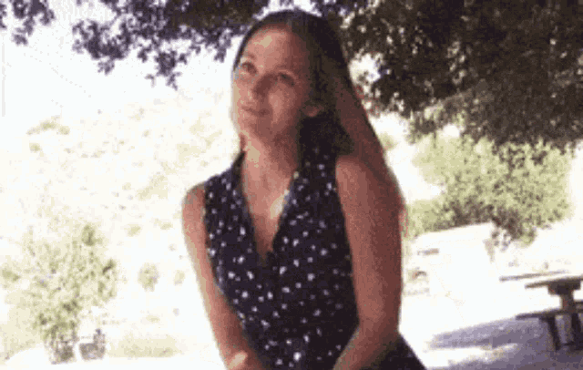 a woman in a blue polka dot dress is standing under a tree .
