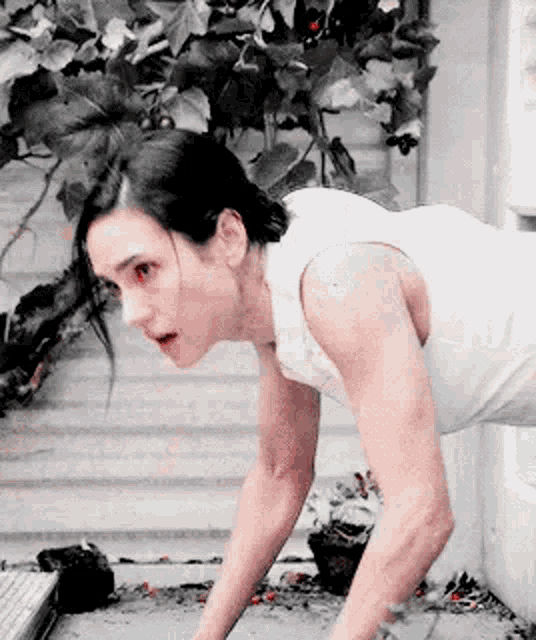 a woman in a white tank top is doing push ups on the floor .