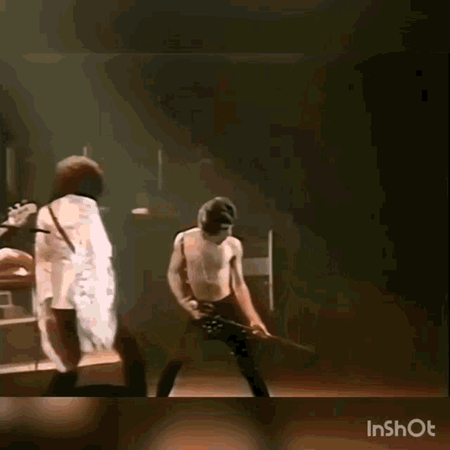 a man without a shirt is playing a guitar on a stage with another man .