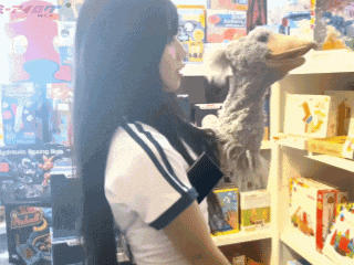 a woman holding a stuffed animal in front of a shelf that says ' toys '
