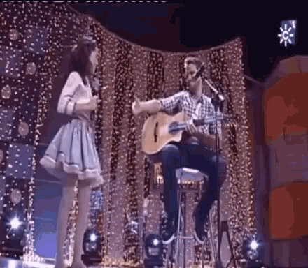 a man playing a guitar and a woman singing into a microphone on a stage .