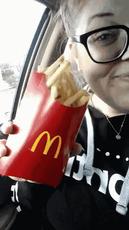a woman wearing glasses is holding a large mcdonald 's bag of french fries