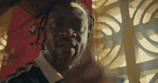 a close up of a man 's face with dreadlocks in front of a window