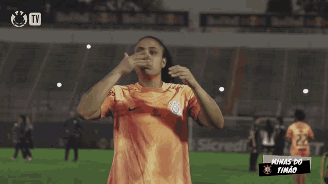 a female soccer player stands on a field in front of a tv screen that says minas do timao