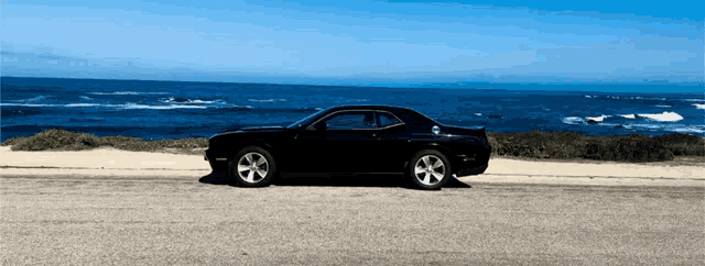 a black car is parked on a road near the ocean