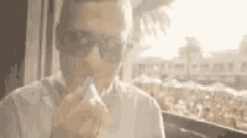 a man wearing sunglasses is smoking an electronic cigarette while sitting at a table .