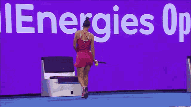 a woman in a red dress is holding a tennis racquet in front of a purple sign that says energies op