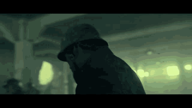 a man wearing a hat is standing in a dark room looking down .