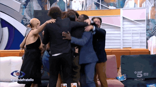 a group of people hugging each other in front of a sign that says #grandefratello