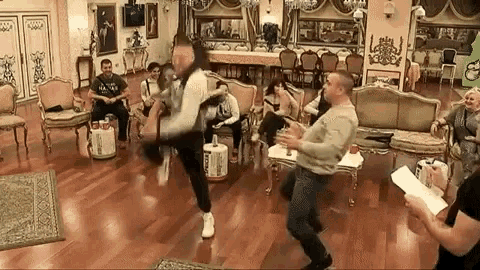 a group of people are dancing in a living room while a man kicks another man .