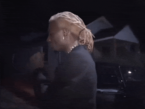 a man with blonde hair and dreadlocks is wearing a black suit and earrings .