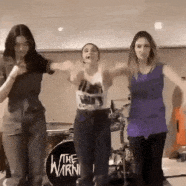 three women are dancing in front of a drum set that says the warning
