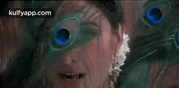 a close up of a woman 's face with a peacock feather in her eyes .