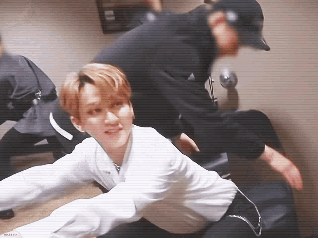 a man in a white shirt is laying on the floor next to another man in a black hat