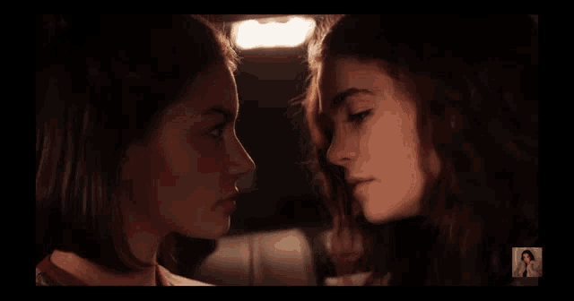 two girls are looking at each other in a dark room with a picture of a woman in the corner