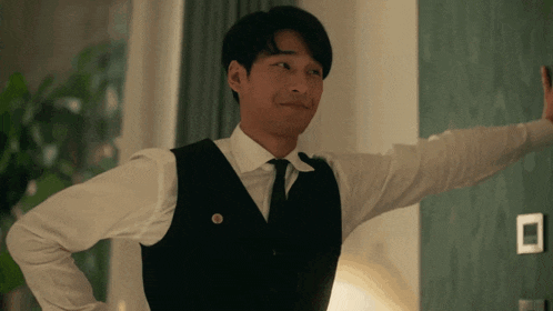 a man in a vest and tie is standing in a room with his arm outstretched