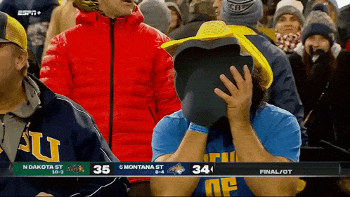 a man wearing a cowboy hat covers his face while watching a football game