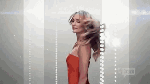 a woman in a red dress is standing in front of a wall with her hair blowing in the wind .