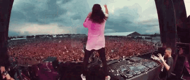 a woman in a pink shirt is standing on a stage in front of a crowd at a concert .