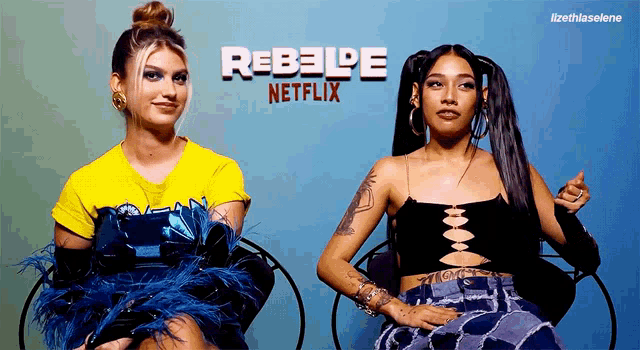 two women are sitting next to each other in front of a rebelde netflix poster