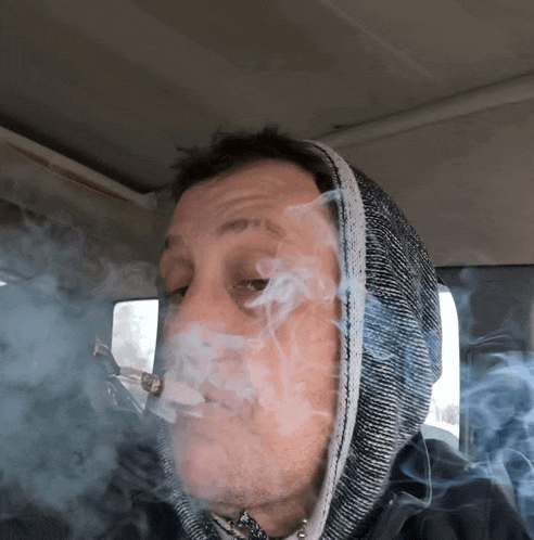 a man wearing a hooded jacket is smoking a pipe