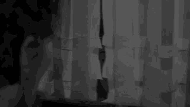 a black and white photo of a woman peeking out of a window .