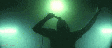 a man is singing into a microphone in a dark room with a green light behind him .
