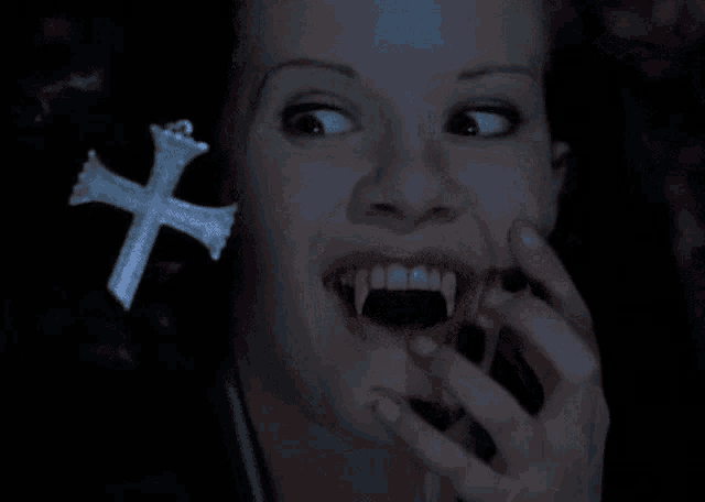 a woman with vampire teeth holds a cross in her hand