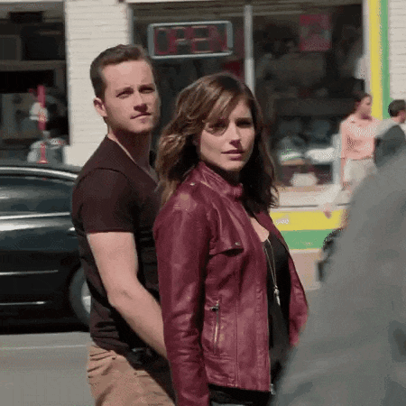 a man and a woman are walking down a street in front of a store that says open .