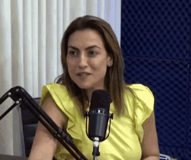 a woman wearing a yellow top is sitting in front of a microphone