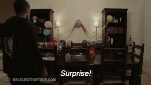 a man is standing in front of a table with balloons and the words surprise written on it
