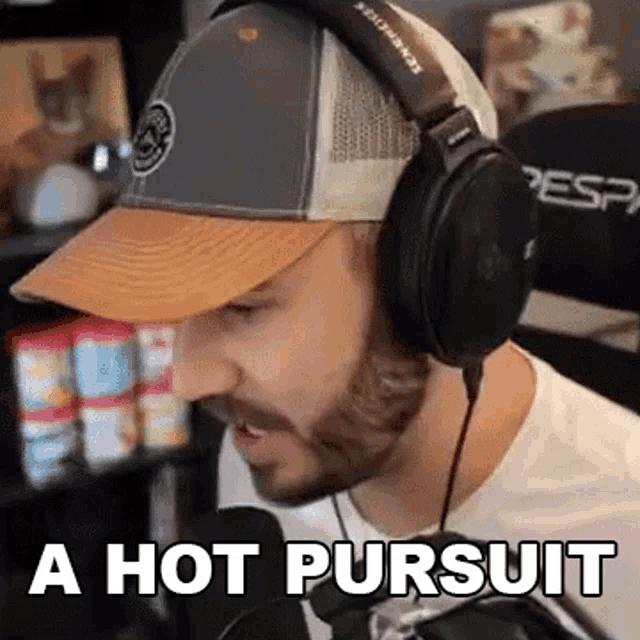 a man wearing headphones and a hat is talking into a microphone and saying `` a hot pursuit '' .