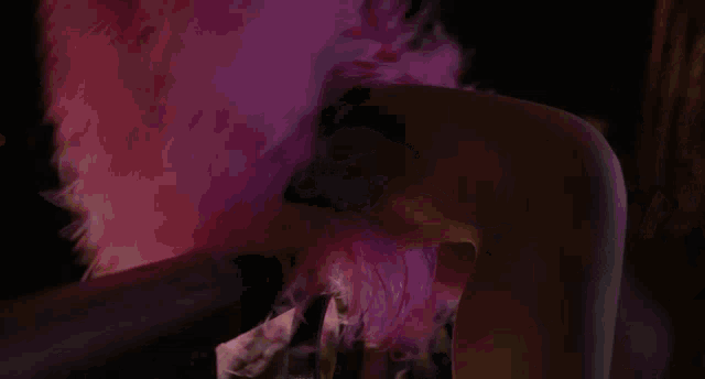 a woman is wearing a pink feathered dress and dancing in a dark room .