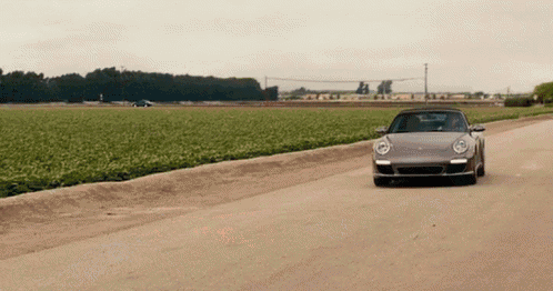 a silver sports car is driving down a dirt road next to a field